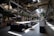 A spacious, modern office interior with high ceilings and large windows allowing natural light to illuminate the space. The area is filled with rows of white office chairs and long wooden tables. Lush green plants are strategically placed around the office, adding a touch of nature. Industrial elements such as exposed beams and metal structures are visible. Various office supplies and board games are placed on the tables.