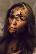 A woman gazes intently, adorned with colorful butterfly stickers across her face, creating an artistic and surreal effect. Her hair cascades around her shoulders, highlighted by soft lighting that adds warmth to the scene.