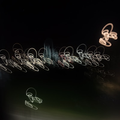 Abstract light trails form circular patterns against a dark background, resembling chaotic scribbles or loops with varied brightness.