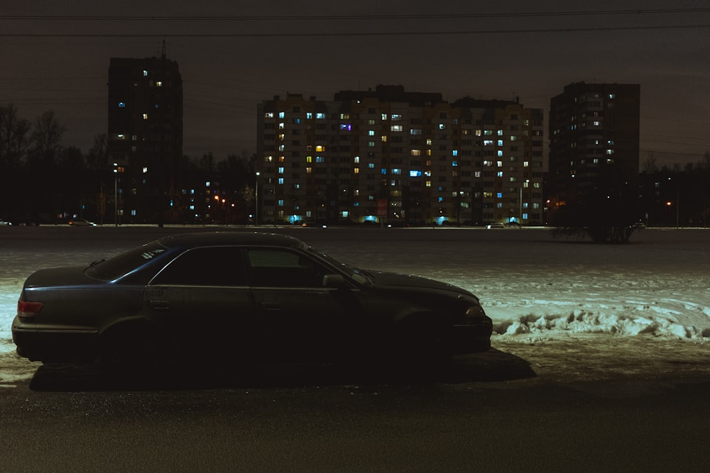 a car parked in the snow in front of a city at night