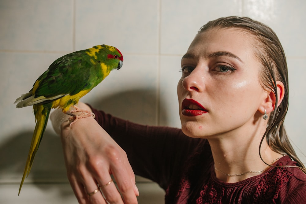 a woman holding a green and yellow bird in her hand