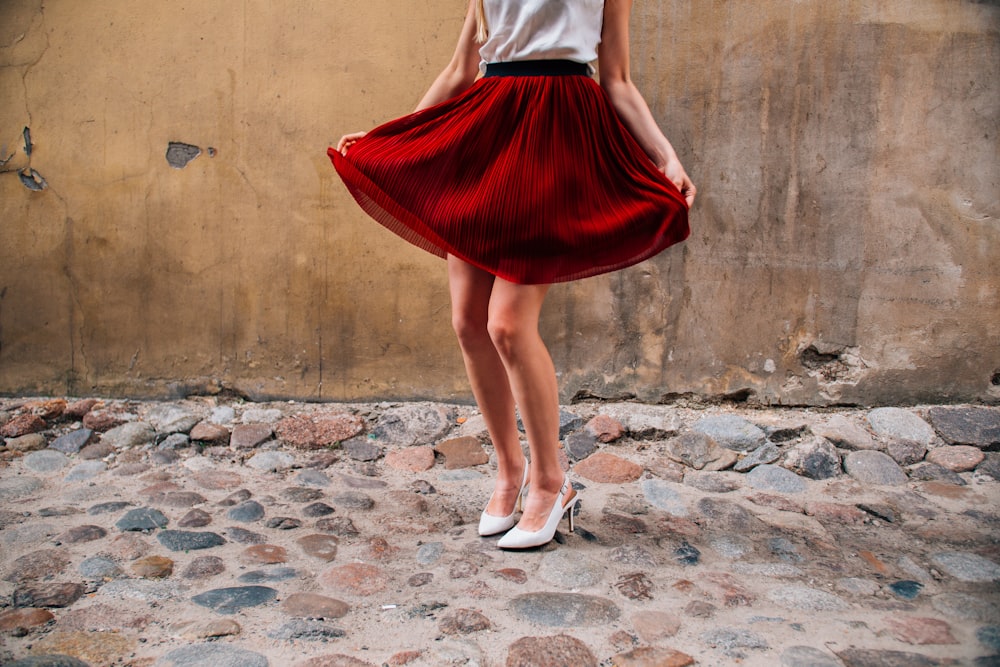 a woman in a red pleated skirt stands on a cobblestone street