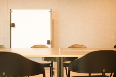 A meeting room with a large conference table surrounded by several black chairs. A whiteboard is mounted on the wall in the background, providing a professional setting.