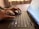 Hands typing on a laptop keyboard with a portion of the screen showing a web page. The background includes a curtain and some stationery items.