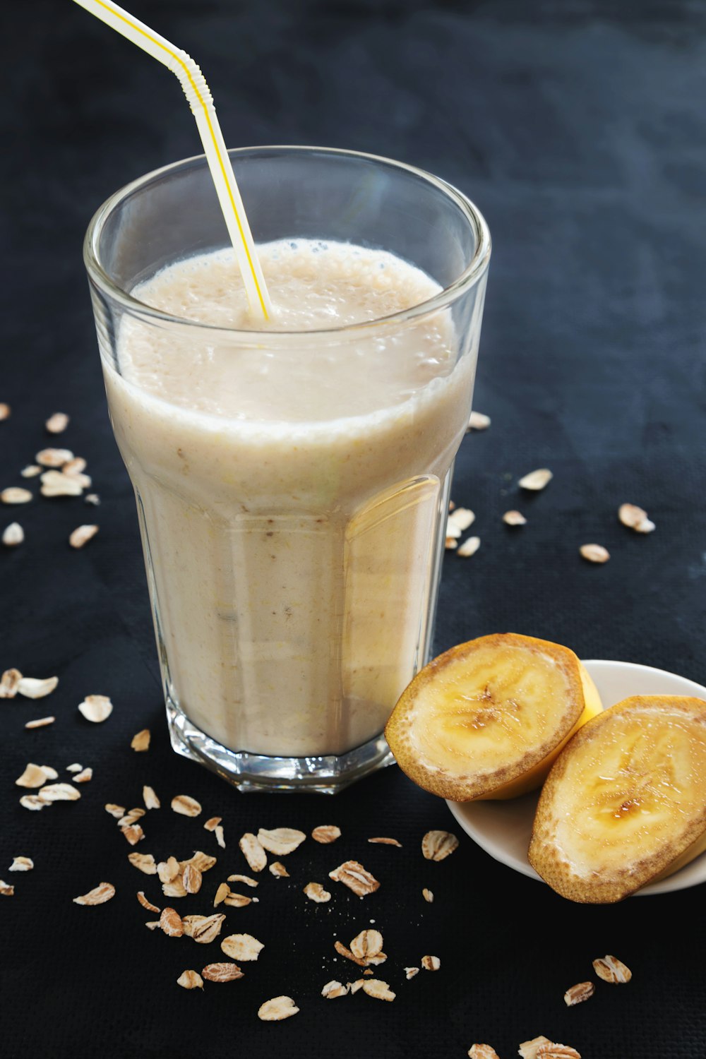 a banana smoothie in a glass next to a plate of sliced bananas