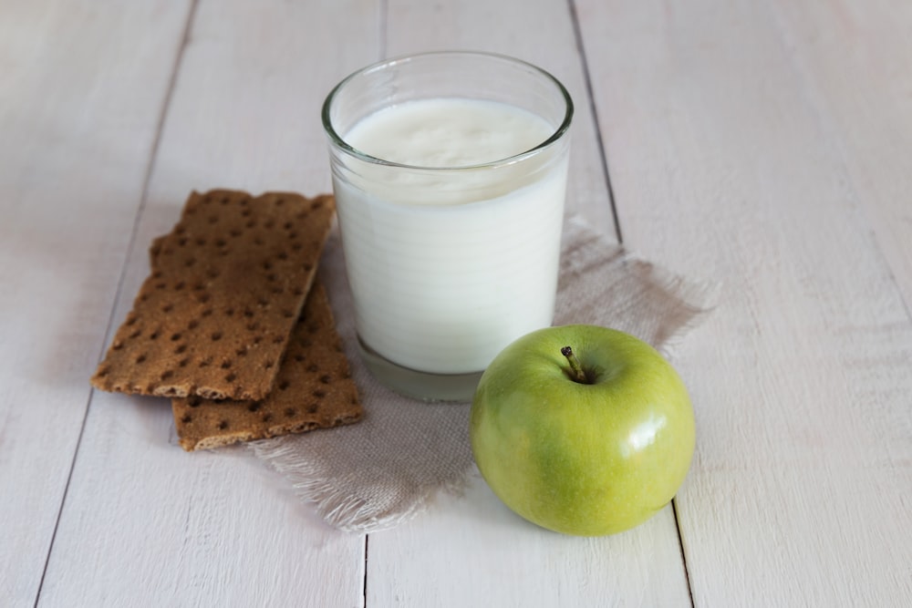a glass of milk, crackers and an apple on a table