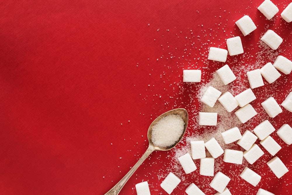 des morceaux de sucre et une cuillère sur une surface rouge