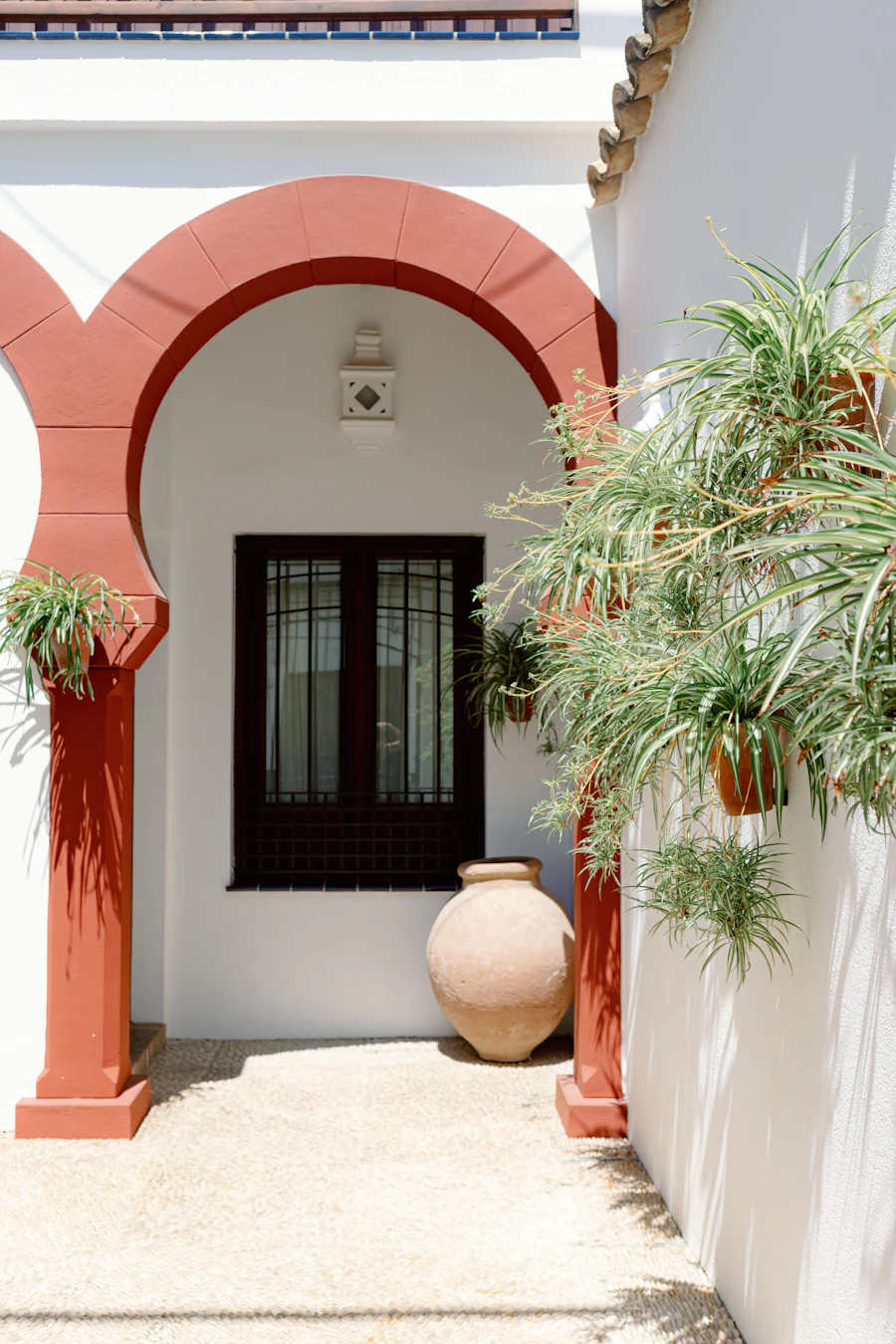 A white house with a red arch and a large potted plant
