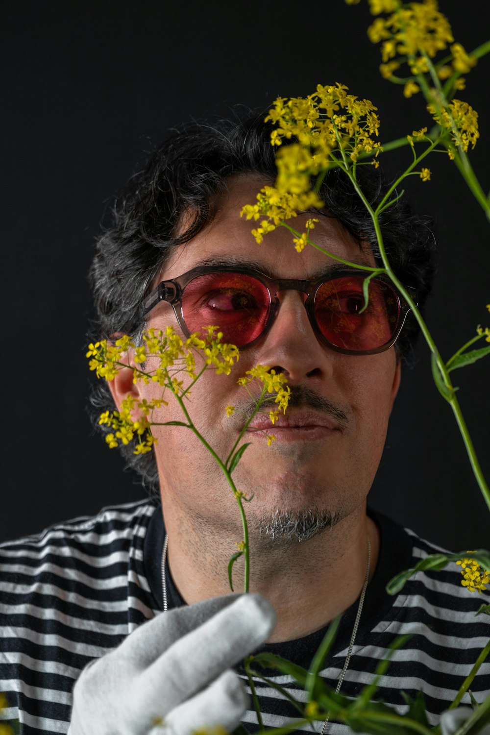 a man in a striped shirt and white gloves holding a bunch of yellow flowers