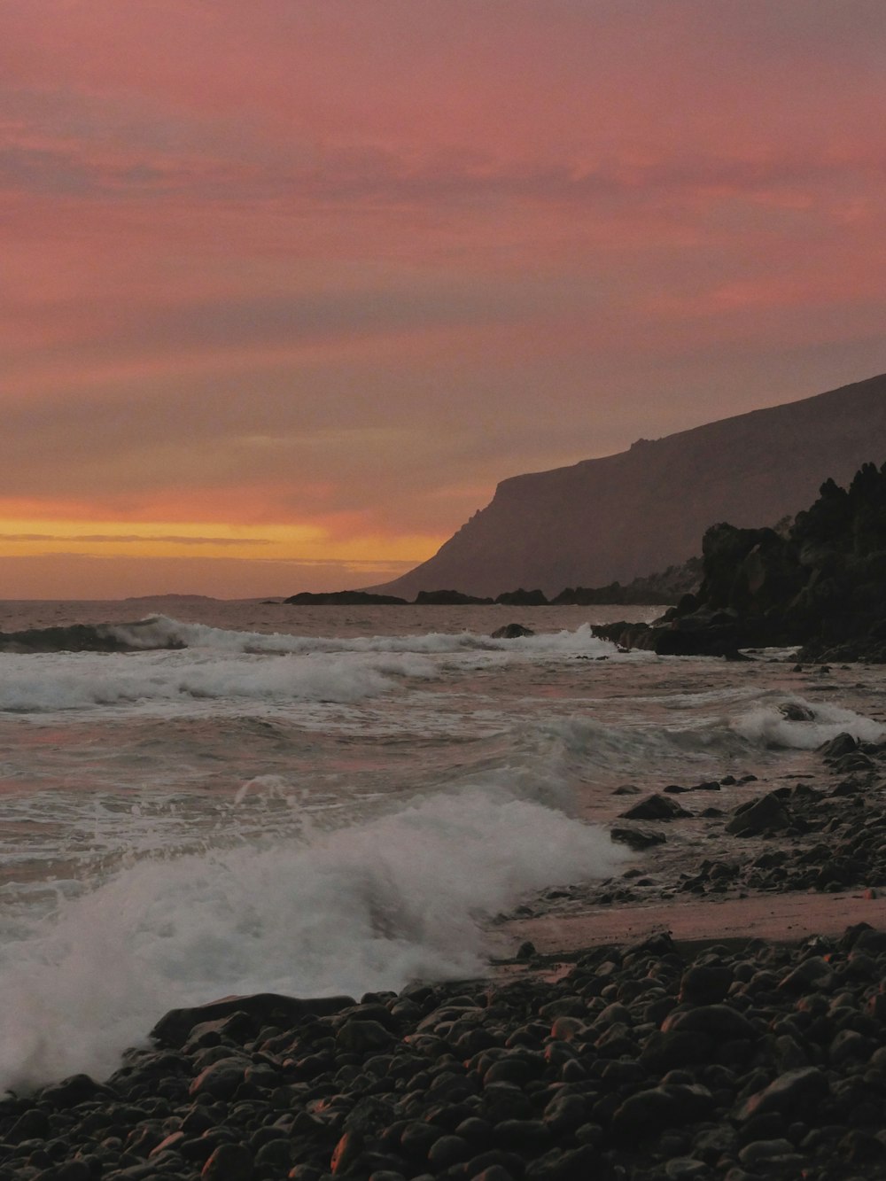 a sunset view of a rocky beach with waves coming in