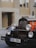 An antique black and orange car is parked on a street with a background of beige buildings. The front of the car features large, round headlights and a chrome radiator grille. A European license plate with the initials 'CZ' and the number '6AN 3564' is attached to the front bumper.