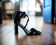 Artistic photo of black minimalist sandals on light-colored wooden flooring.