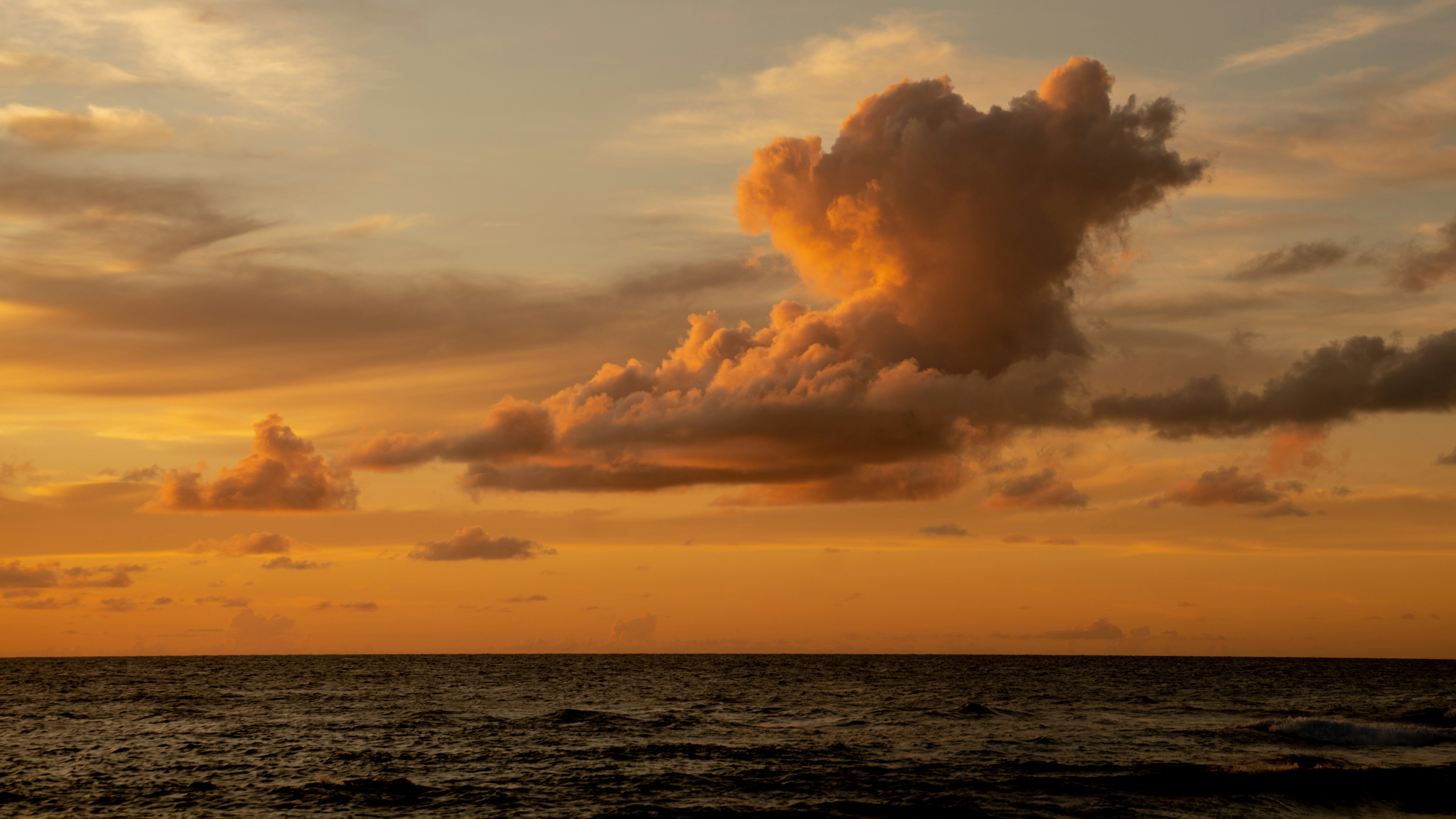 the sun is setting over the ocean with clouds in the sky