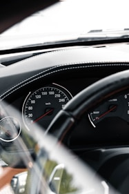 A close-up view of a car's dashboard, featuring a speedometer and tachometer. The speedometer shows a range from 0 to 260 km/h, while the tachometer provides RPM measurements. The dashboard is black with subtle stitching details, and there's a steering wheel partially visible in the foreground.