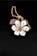 A gold chain necklace features a pendant shaped like a flower with white petals adorned with small green gems. At the center of the flower is a larger yellow gem. Behind the flower, a dark textured stone adds contrast to the composition. The background is a smooth, black surface that enhances the details of the jewelry.