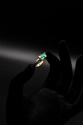 a person's hand holding a ring with a green stone