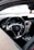 The interior of a luxury car featuring a sleek steering wheel with a chrome Mercedes-Benz logo at the center. The dashboard includes digital displays and air vents with metallic accents. A small screen is mounted on the center console, and a decorative Fanta air freshener hangs from the rear-view mirror.