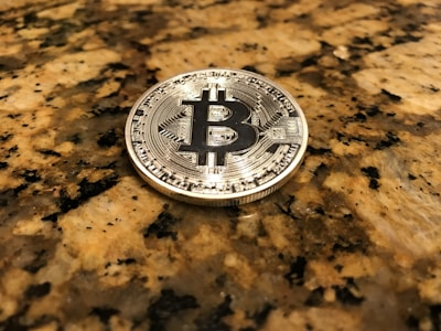 A physical Bitcoin coin placed on a polished, speckled granite surface. The coin, with its intricate design, reflects light, creating a shiny effect against the earth-toned countertop.