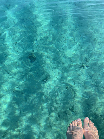 Close-up of a traveler’s feet dipping into crystal-clear ocean water near colorful coral reefs.