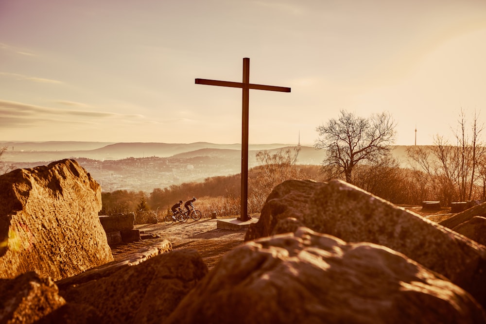 a cross on top of a mountain with a person on a bike in the background