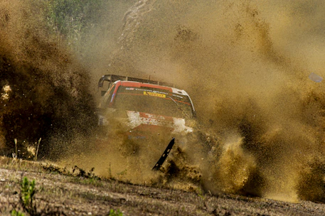 Action shot of the Cambodia Rally Team's car kicking up dust on a rugged dirt trail.
