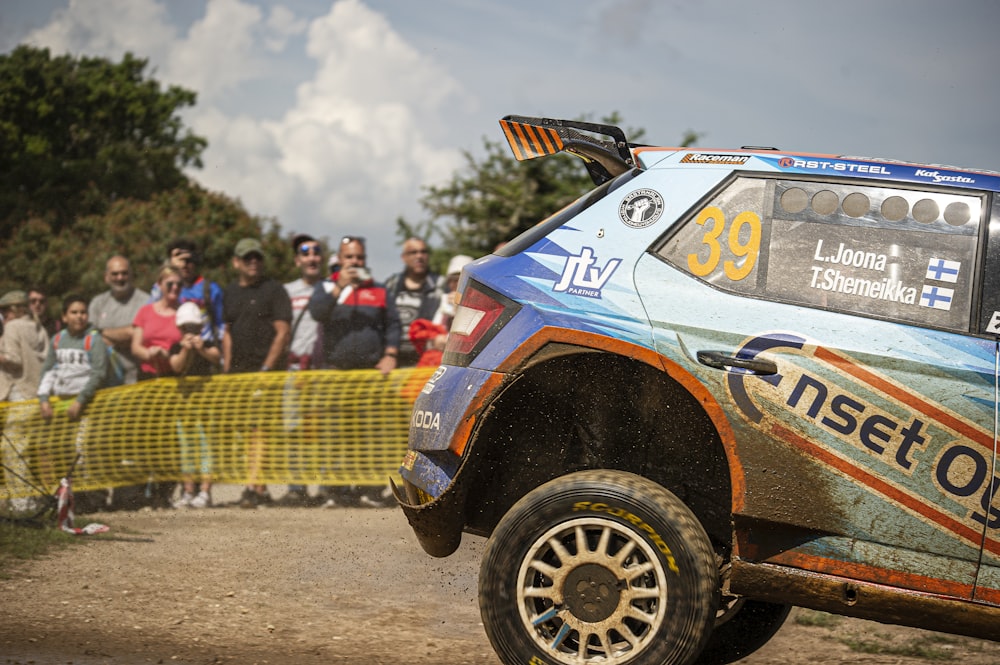 a rally car driving down a dirt road in front of a crowd