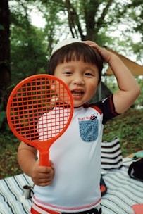 A group of smiling children holding tennis rackets on a sunny court.