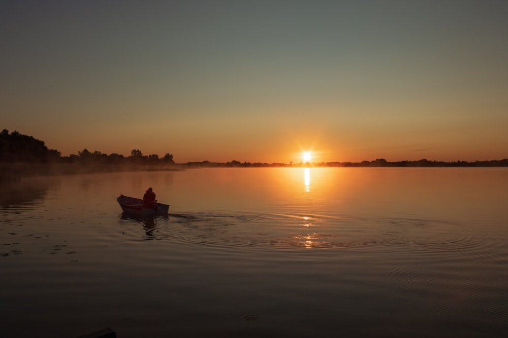 a person in a small boat on a lake at sunset
