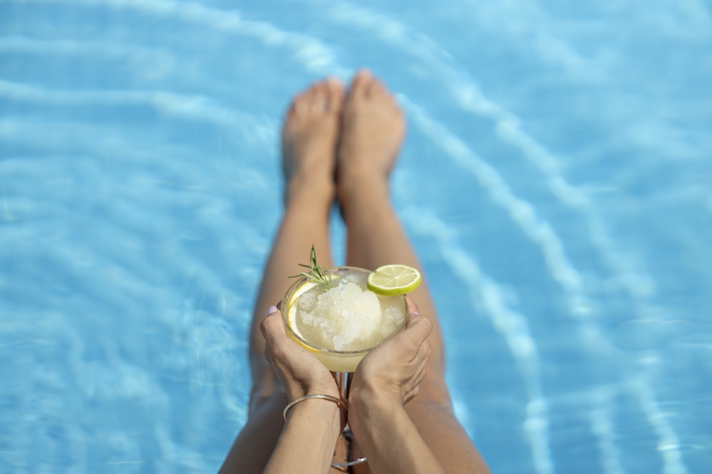 a person holding a drink in their hand near a pool