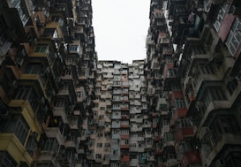 A dense cluster of high-rise apartment buildings with numerous windows and balconies, creating a feeling of urban confinement. The architecture appears aged with varying shades of gray, red, and cream, giving a sense of wear and history.