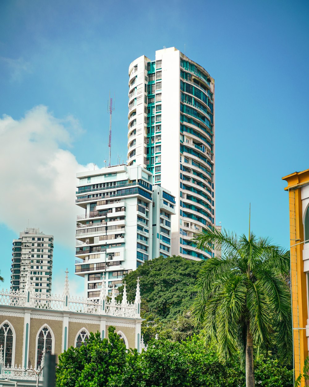 a tall white building sitting next to a lush green forest