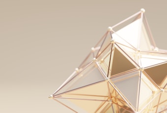 A geometric structure with a complex arrangement of interconnected triangular shapes. The design features metallic edges and reflective surfaces, creating a sophisticated and modern appearance on a muted beige background.