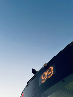 A friendly driver greeting passengers next to a clean, well-maintained bus under a bright sky.