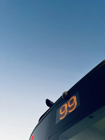 A friendly driver helping passengers board a clean, modern bus under a bright sky.
