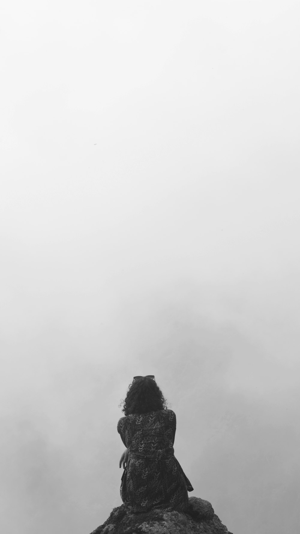 a black and white photo of a person sitting on a rock