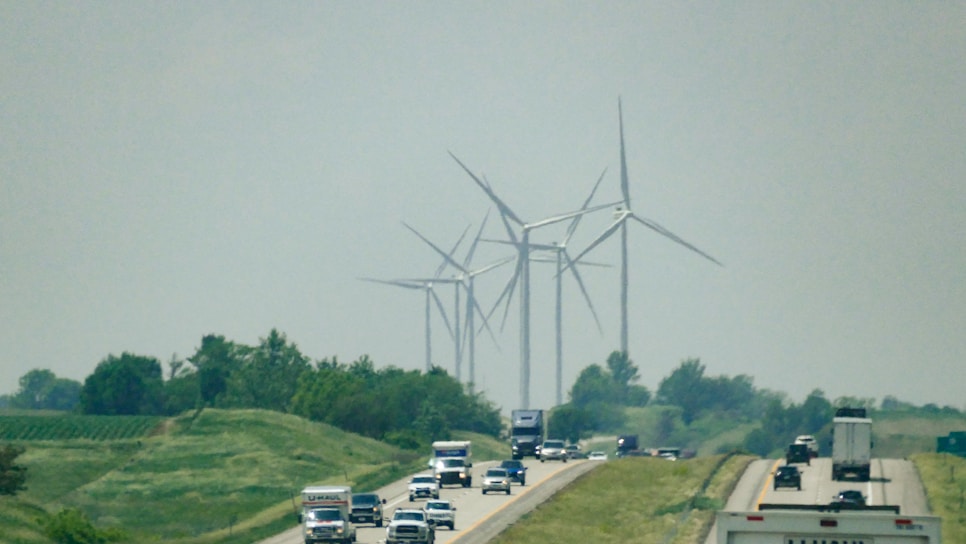 A large truck transporting wind turbine components on a highway surrounded by green fields.