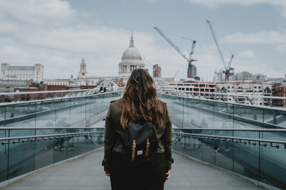 a woman with a backpack walking across a bridge