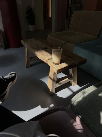 Elegant coffee table with a wooden base and glass top set against a white wall with natural light.