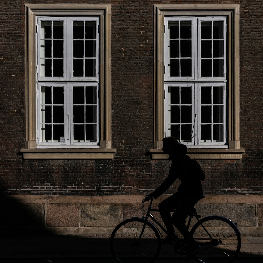 a man riding a bike down a street past two windows