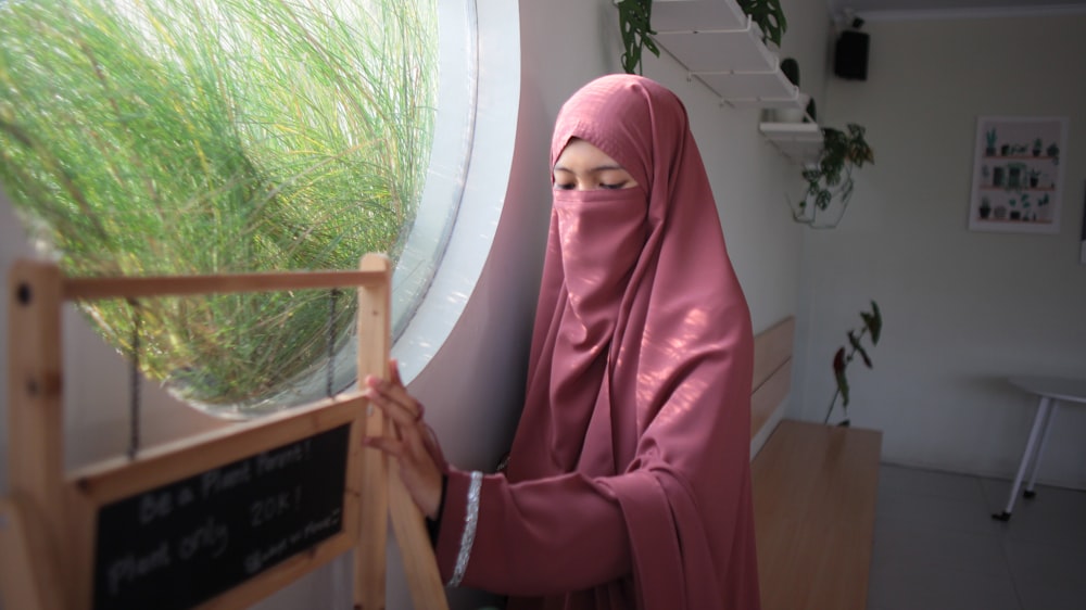 a woman in a pink hijab looking out a window