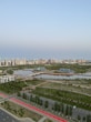 A serene urban landscape featuring high-rise buildings in the background, surrounded by lush greenery and calm water bodies. Solar panels are visible on the banks, indicating a focus on eco-friendly solutions. The area includes paved walkways and well-maintained roads, enhancing accessibility amidst a blend of natural and urban elements.