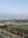 A serene urban landscape featuring high-rise buildings in the background, surrounded by lush greenery and calm water bodies. Solar panels are visible on the banks, indicating a focus on eco-friendly solutions. The area includes paved walkways and well-maintained roads, enhancing accessibility amidst a blend of natural and urban elements.
