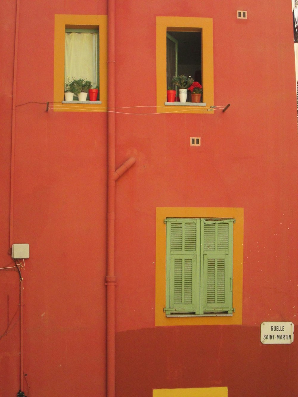 a red building with green shutters and two windows