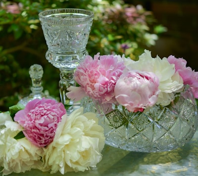 Close-up of a decorative crystal vase filled with fresh white peonies on a dark wood shelf.
