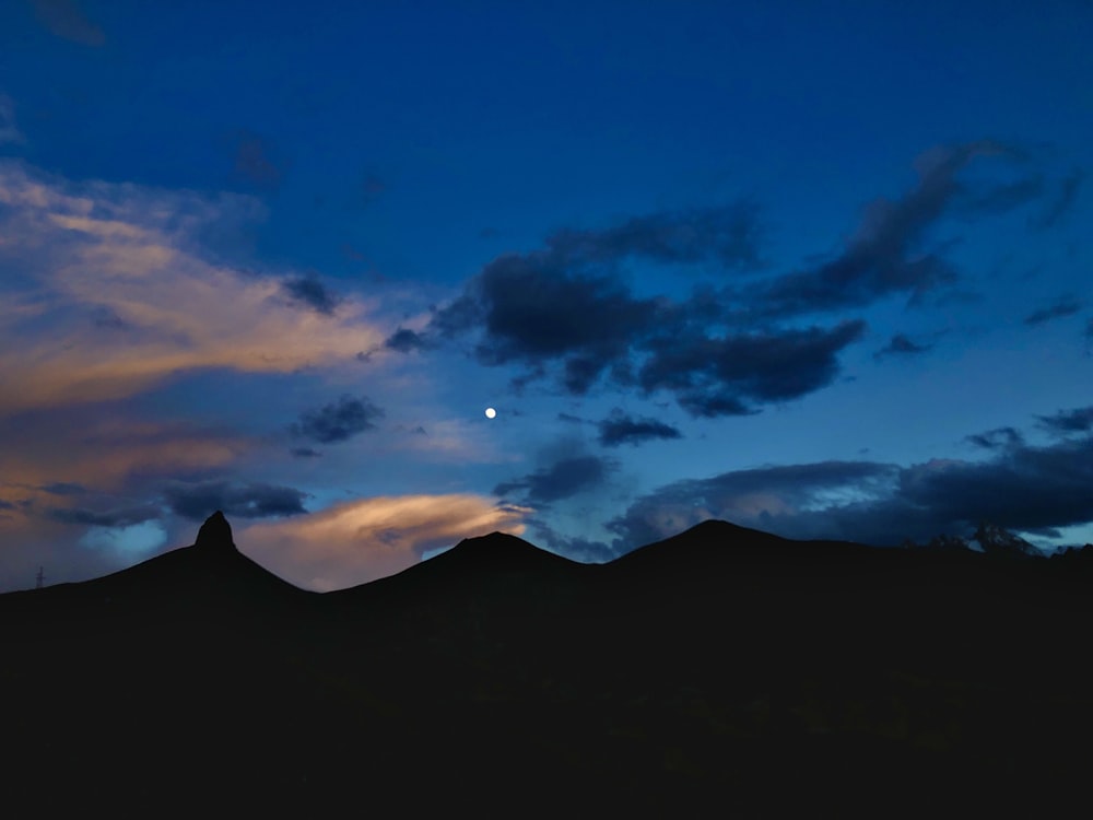 the moon is setting over the mountains in the sky