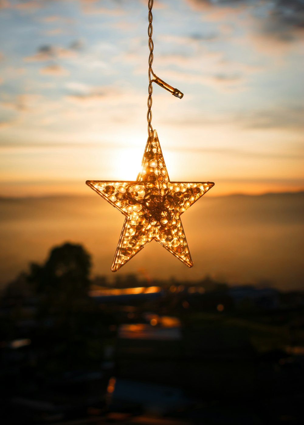 a lighted star hanging from a chain in front of a sunset