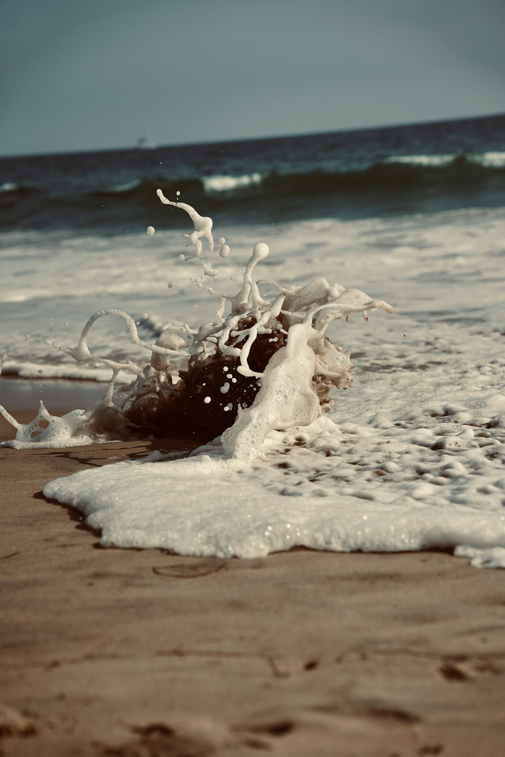 a wave crashing onto a sandy beach next to the ocean