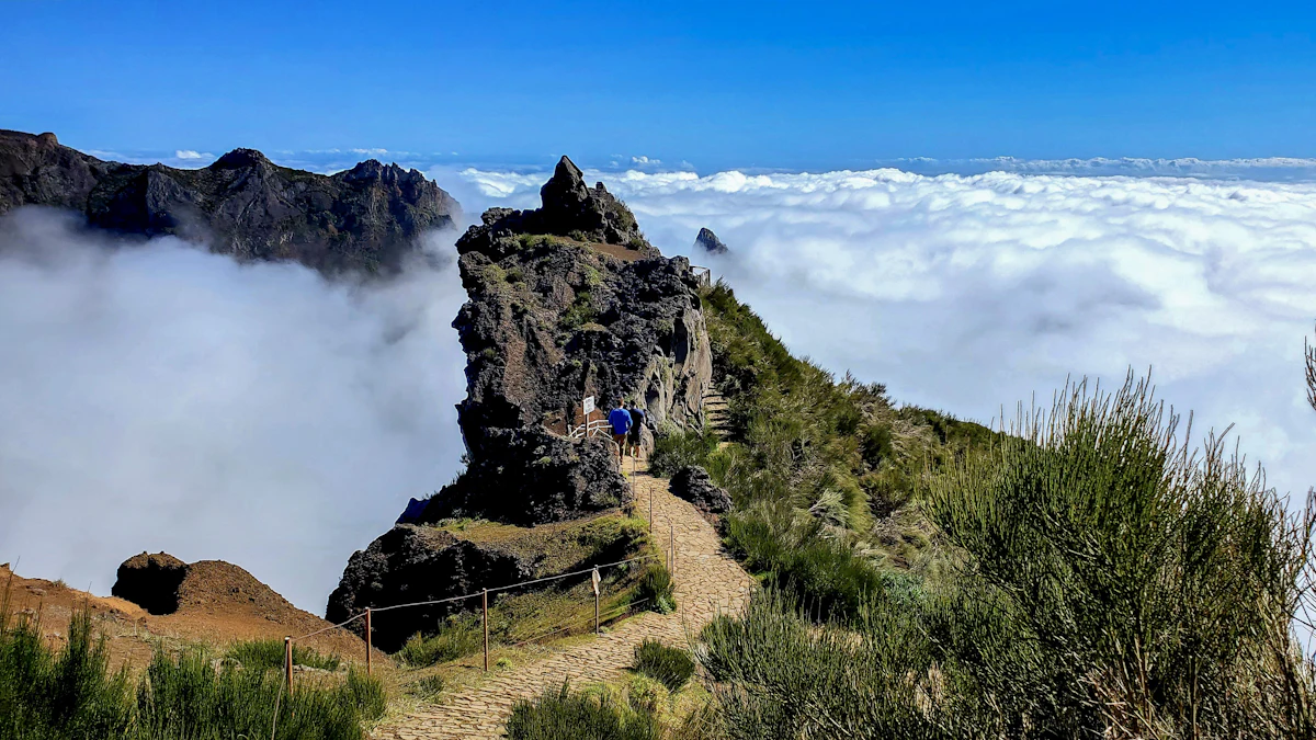 Hikers on the stone path from Pico do Areeiro, with a rock spire and a sea of clouds behind