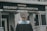 A person wearing a graduation gown and cap is standing in front of a building with the sign 'Gedung Megawati Soekarnoputri'. The image is taken from behind the person, showing the back of their graduation attire. The building appears to be institutional, with grey walls and a somber appearance.