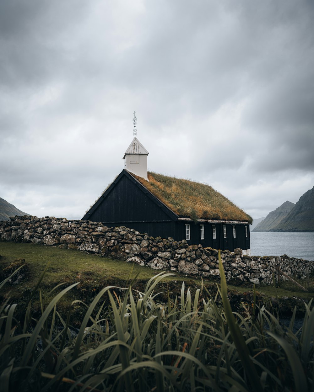 a black building with a grass roof and a white steeple